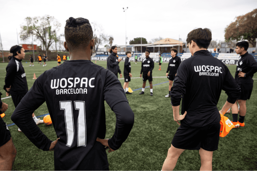 Players wearing black WOSPAC Barcelona kits gathered on a turf field during a training session