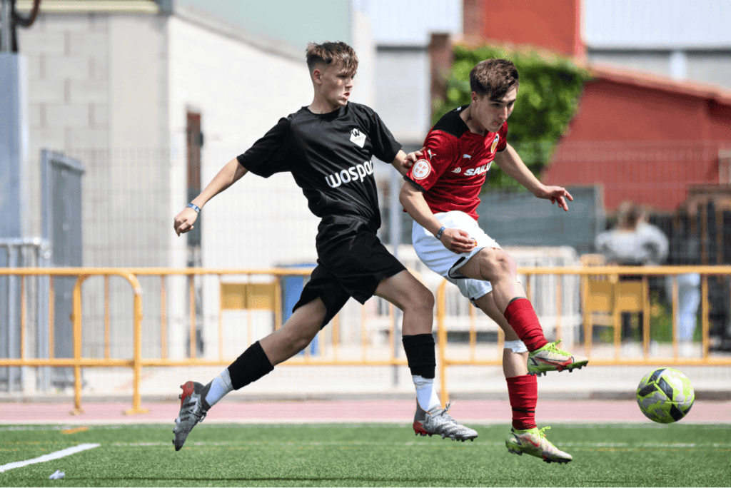 Two youth soccer players competing for a soccer ball during a match on a turf field.