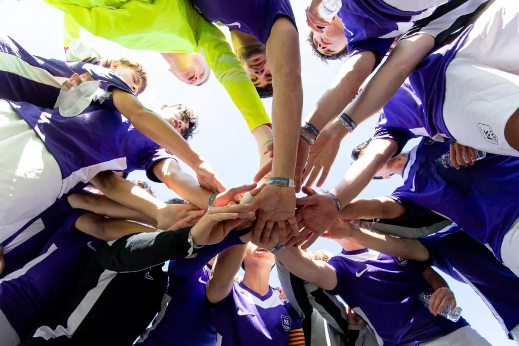 A low-angle shot of a soccer team stacking hands in a team huddle.