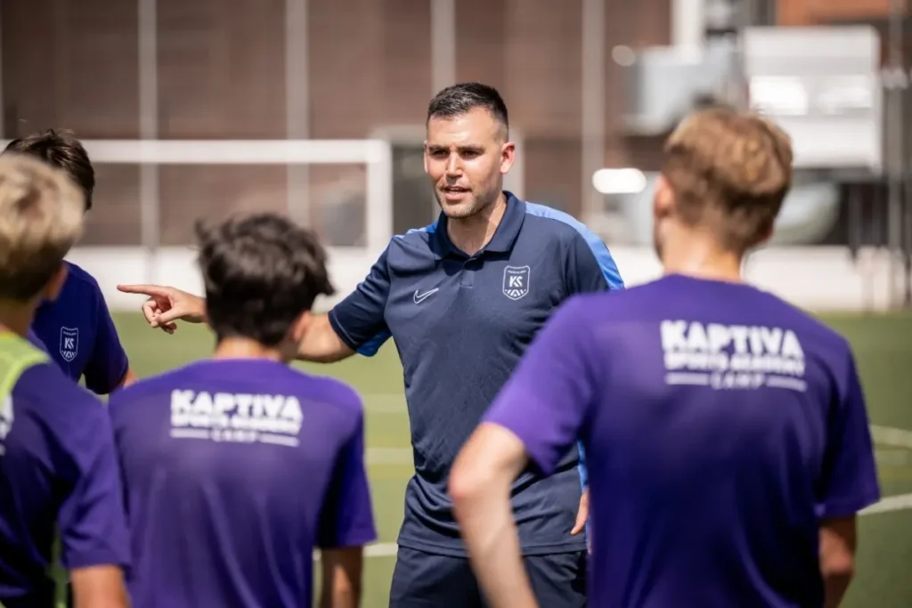 A soccer coach pointing and addressing his team in a huddle on the field.