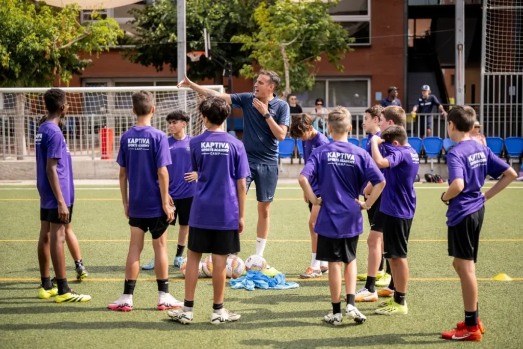 A coach addressing a group of youth soccer players in purple jerseys on an outdoor field.